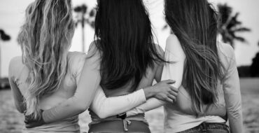 HIgh-calorie Q&A: Three women in jeans and tops bonding at the beach in grayscale.