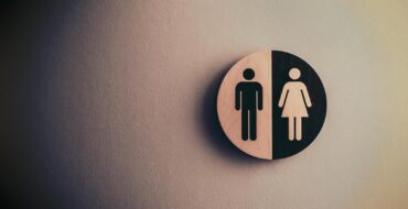 Minimalist gender neutral restroom sign with male and female symbols on textured wall.