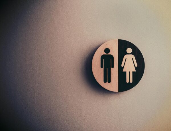 Minimalist gender neutral restroom sign with male and female symbols on textured wall.