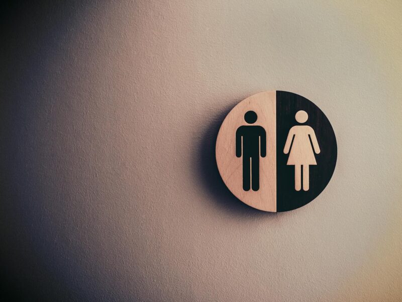 Minimalist gender neutral restroom sign with male and female symbols on textured wall.