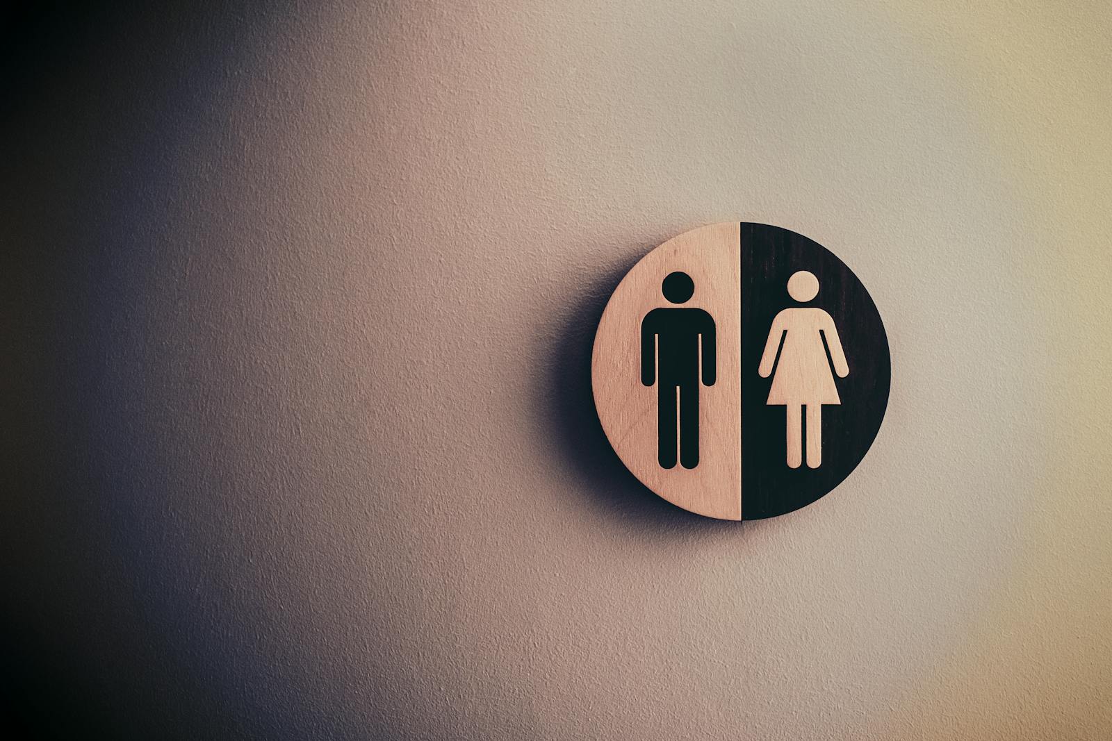 Minimalist gender neutral restroom sign with male and female symbols on textured wall.