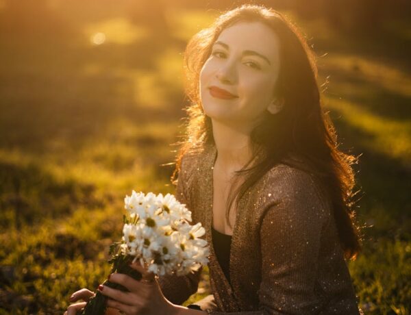 A woman smiles while holding white flowers in a sunlit outdoor setting.