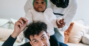 Update article: Cheerful young multiracial parent with curious baby smiling and looking at camera while having fun during weekend at home