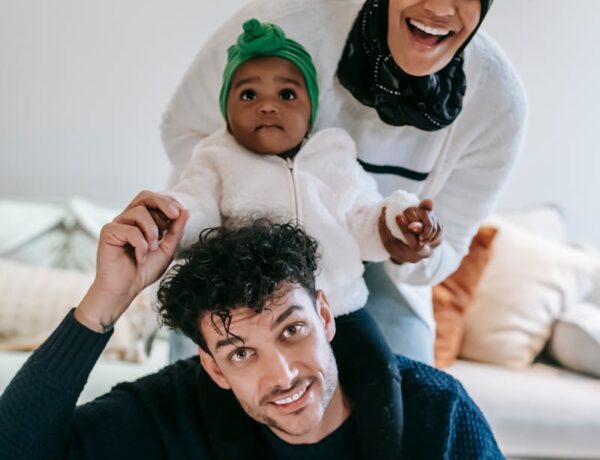 Update article: Cheerful young multiracial parent with curious baby smiling and looking at camera while having fun during weekend at home