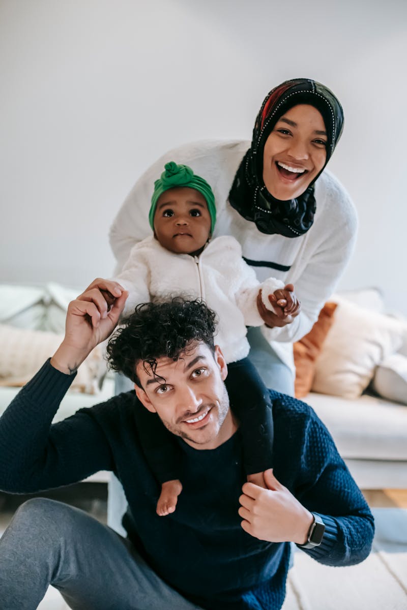 Update article: Cheerful young multiracial parent with curious baby smiling and looking at camera while having fun during weekend at home