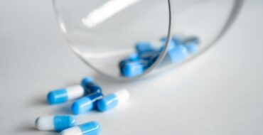 A close-up of blue and white capsules spilling from a glass on a light background.