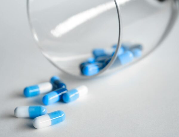 A close-up of blue and white capsules spilling from a glass on a light background.