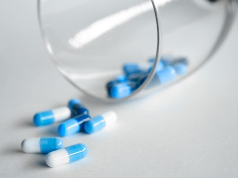 A close-up of blue and white capsules spilling from a glass on a light background.
